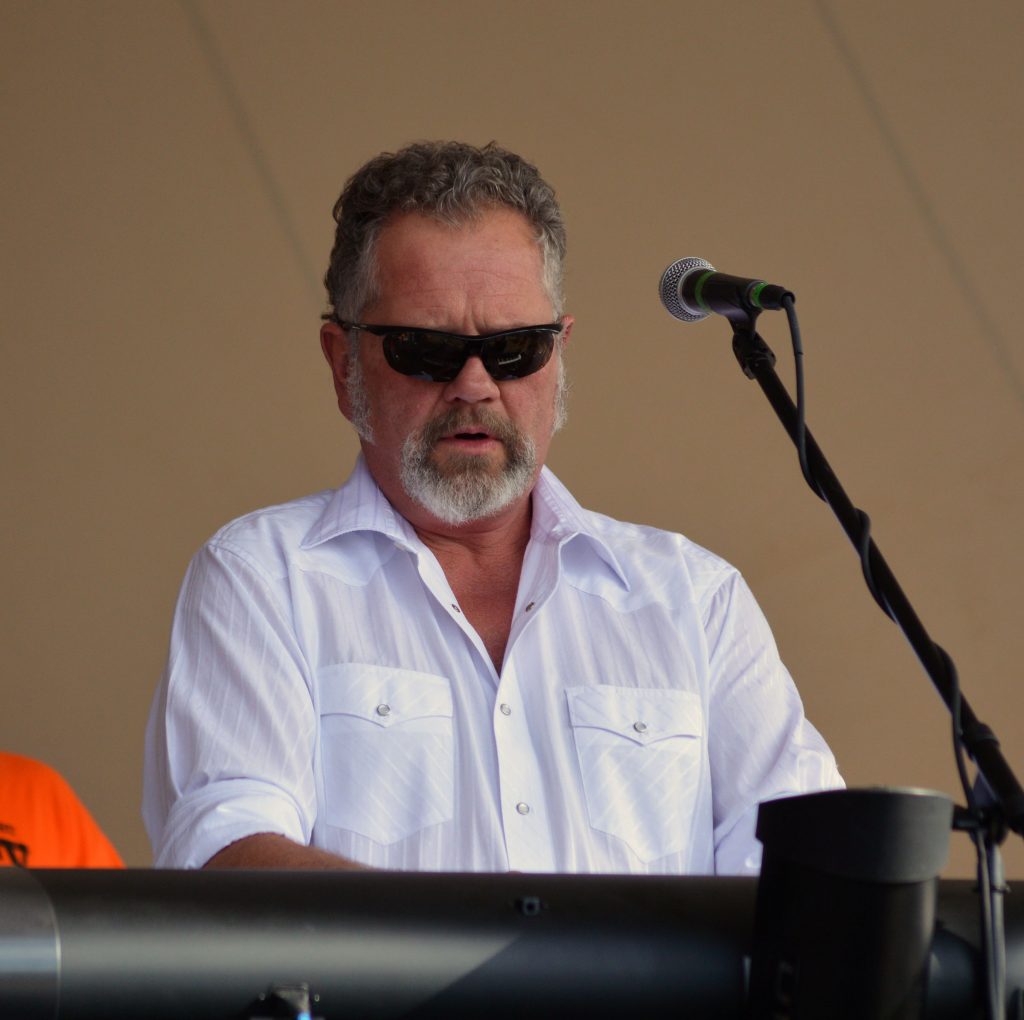 a white man in sunglasses with short salt and pepper hair plays the keyboard